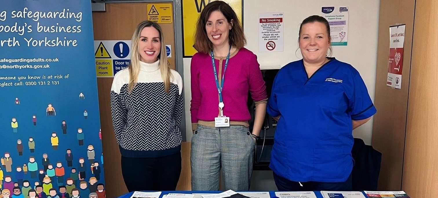 Three women behind a table which is covered with safeguarding leaflets.