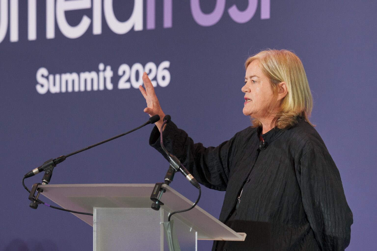 Baroness Casey stands at a podium with her hand gesturing outwards whilst giving a speech. 