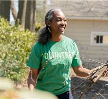 A woman stood outside smiling on a sunny day, wearing a green t-shirt that says "volunteer"